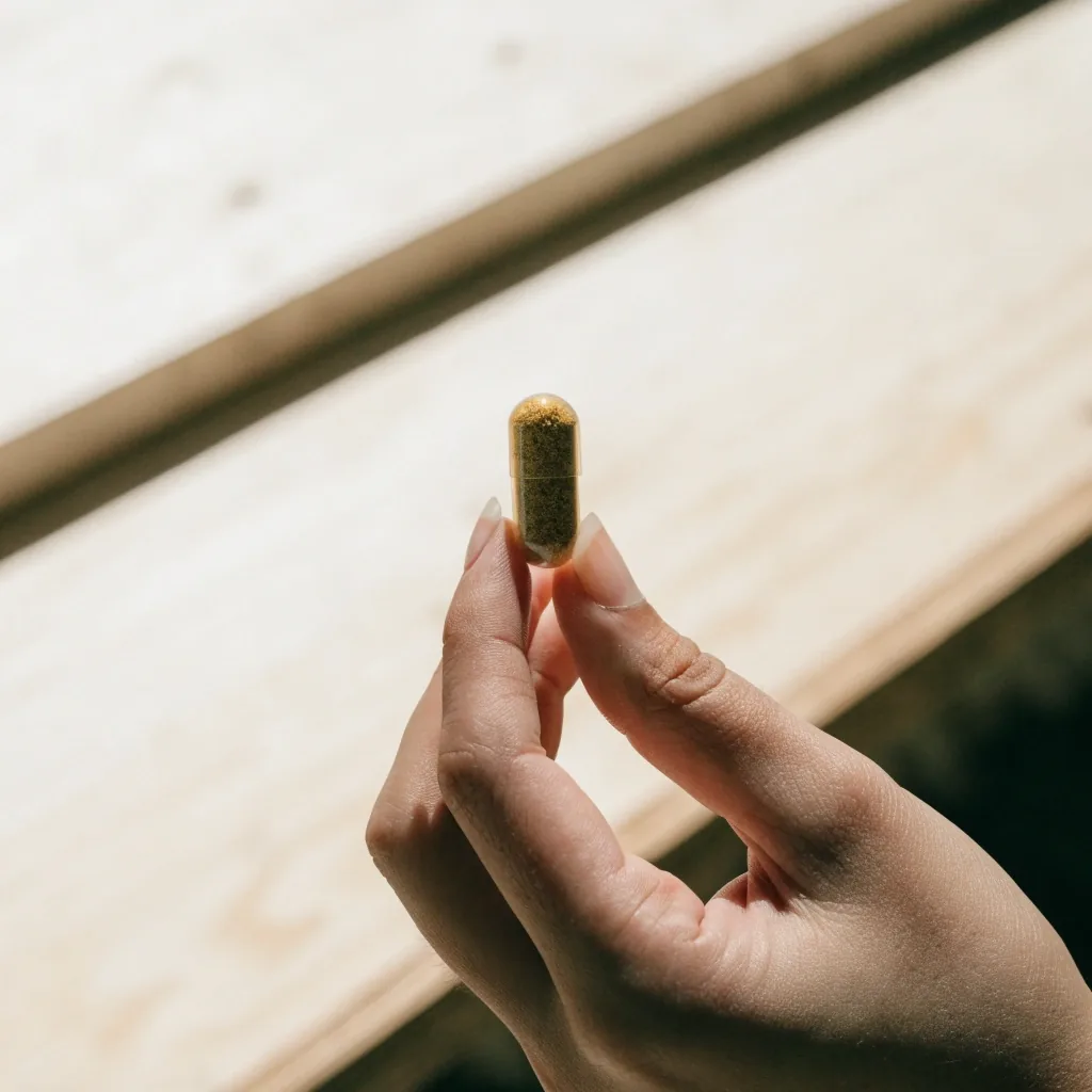 A single translucent herbal capsule held between two fingertips against backlit noon light