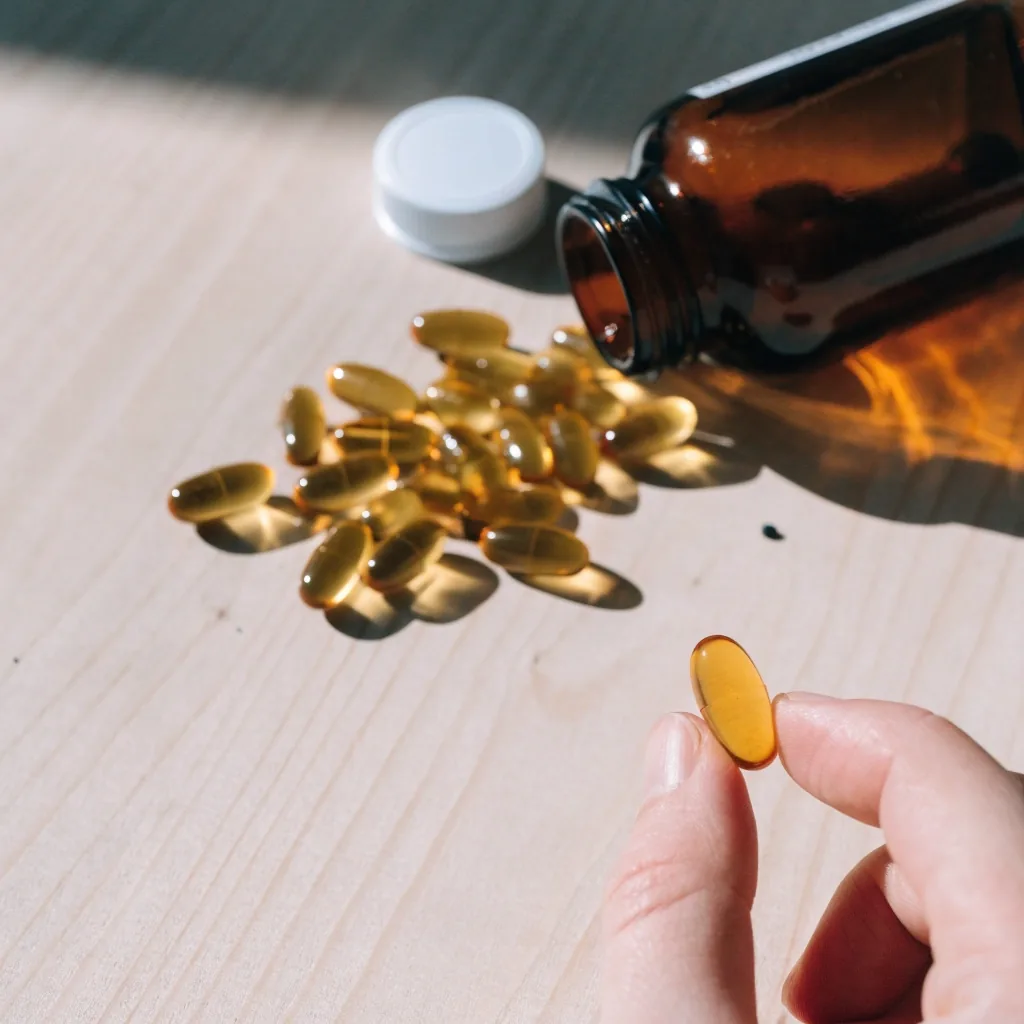A single unmarked capsule held between two fingertips and backlit so the shell reads translucent